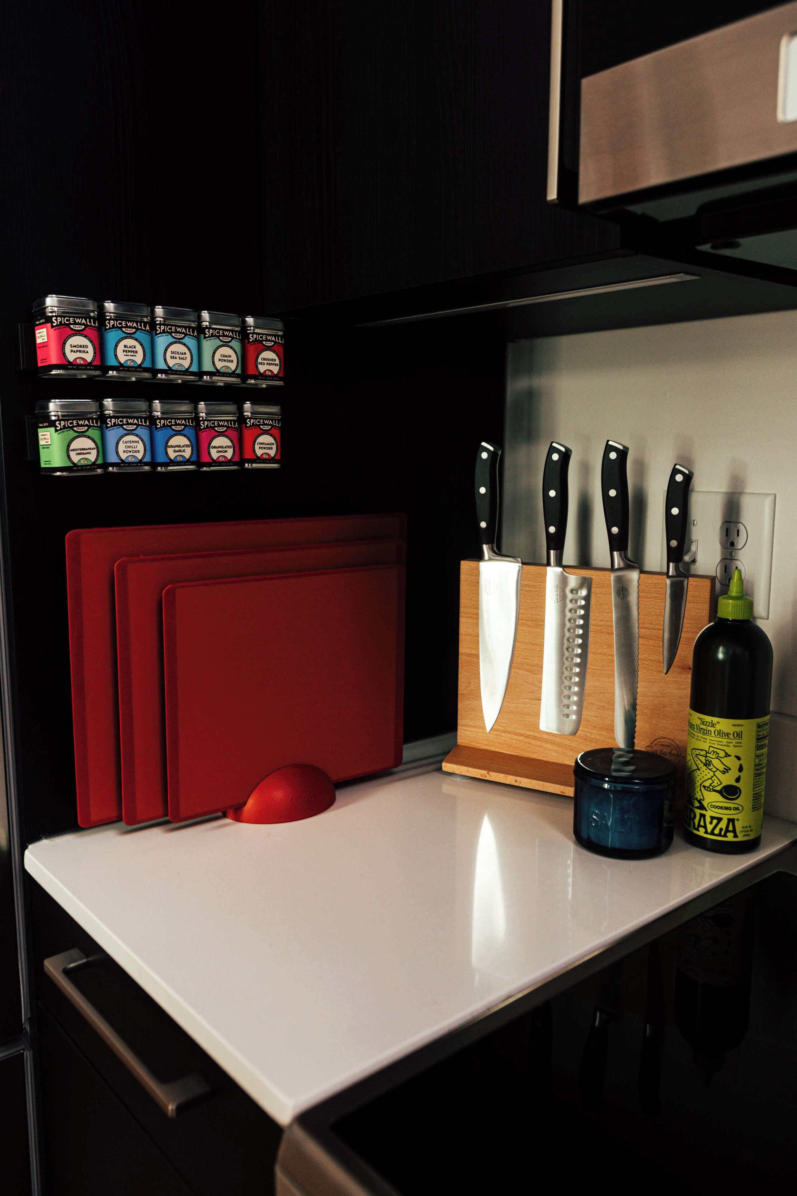 A kitchen counter with a knife block, a red cutting board, and several spice jars.
