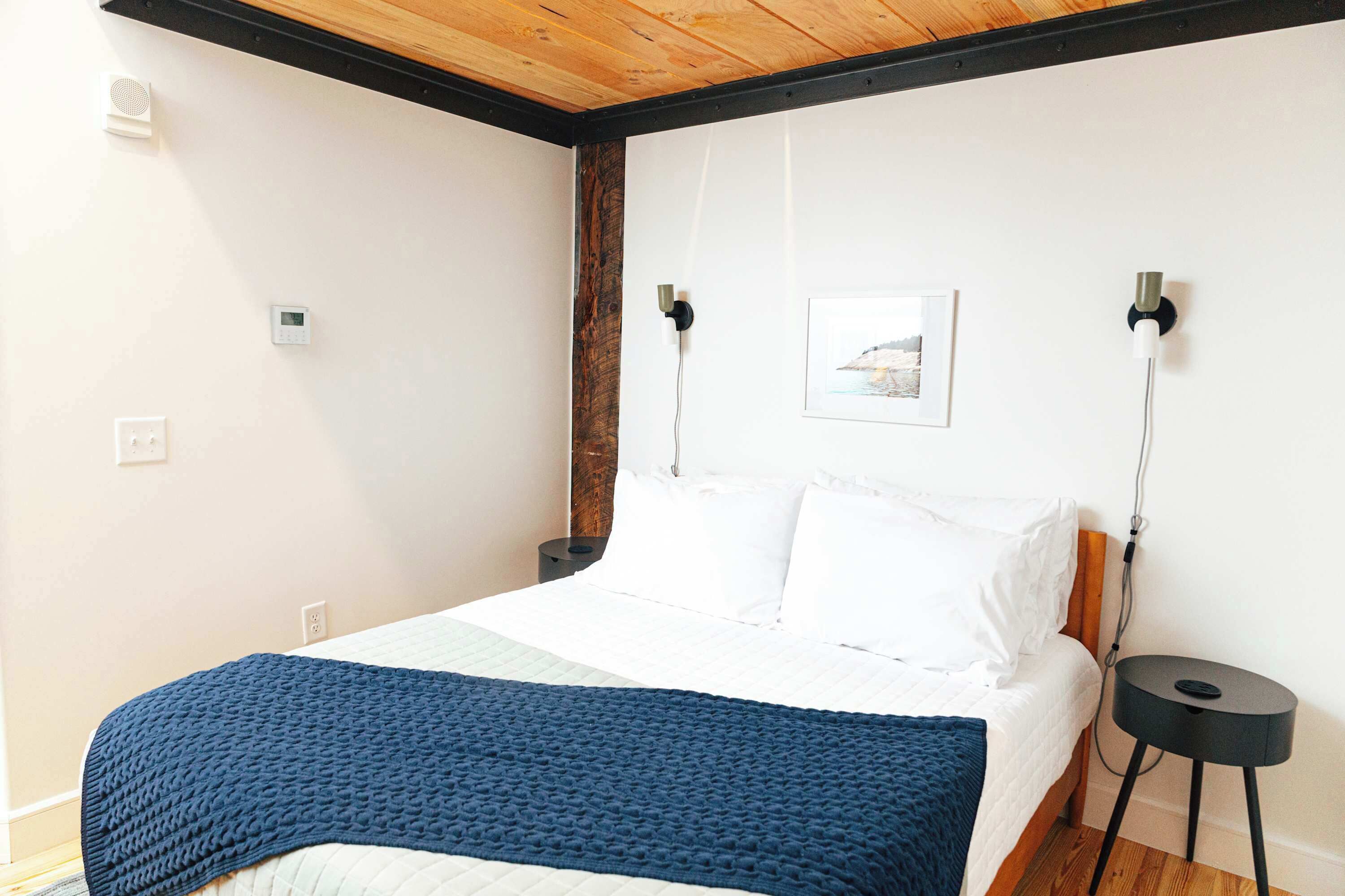 A bedroom with a bed, a bedside table, a wall-mounted light, and a power outlet.