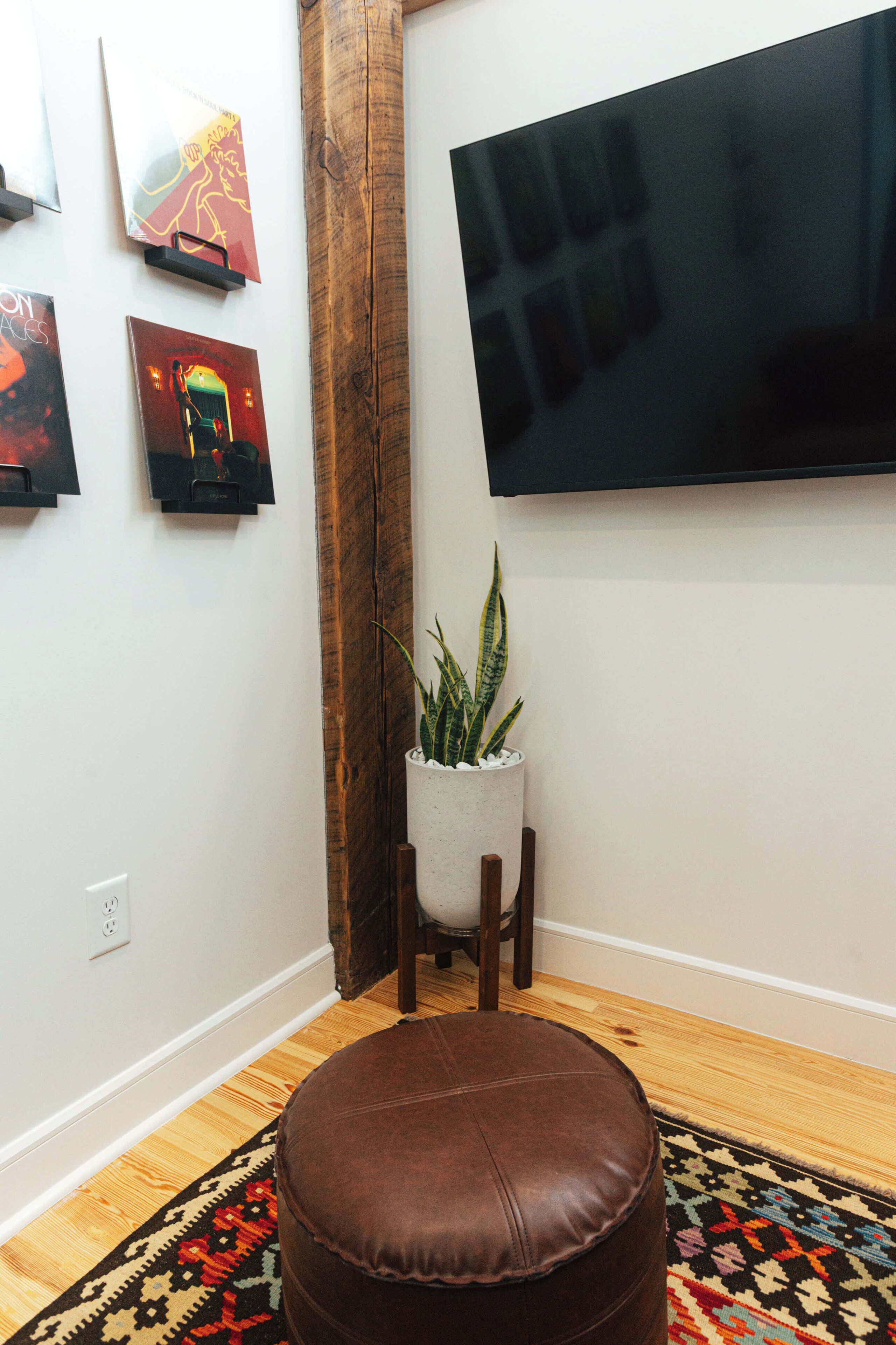 Habitación con un reposapiés de cuero marrón, una planta en maceta y un televisor de pantalla plana montado en la pared.