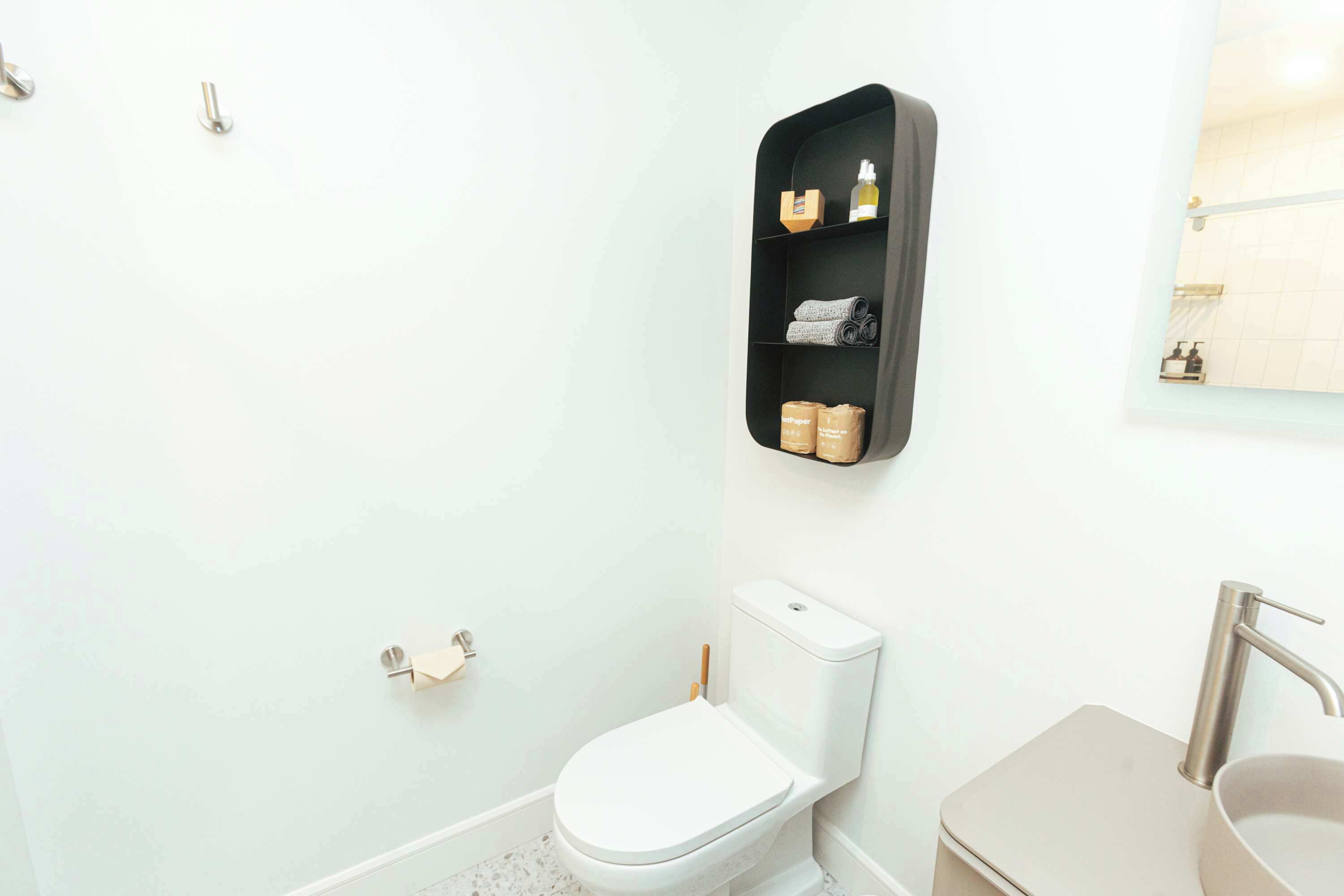 Une salle de bain avec des toilettes blanches, un lavabo et une étagère contenant des articles de toilette.