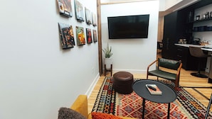 A modern living room with a flat-screen TV, a patterned rug, a brown leather ottoman, and a wooden coffee table. - Loft 305 - The William - Atrium - Live Work Walk (Birmingham)