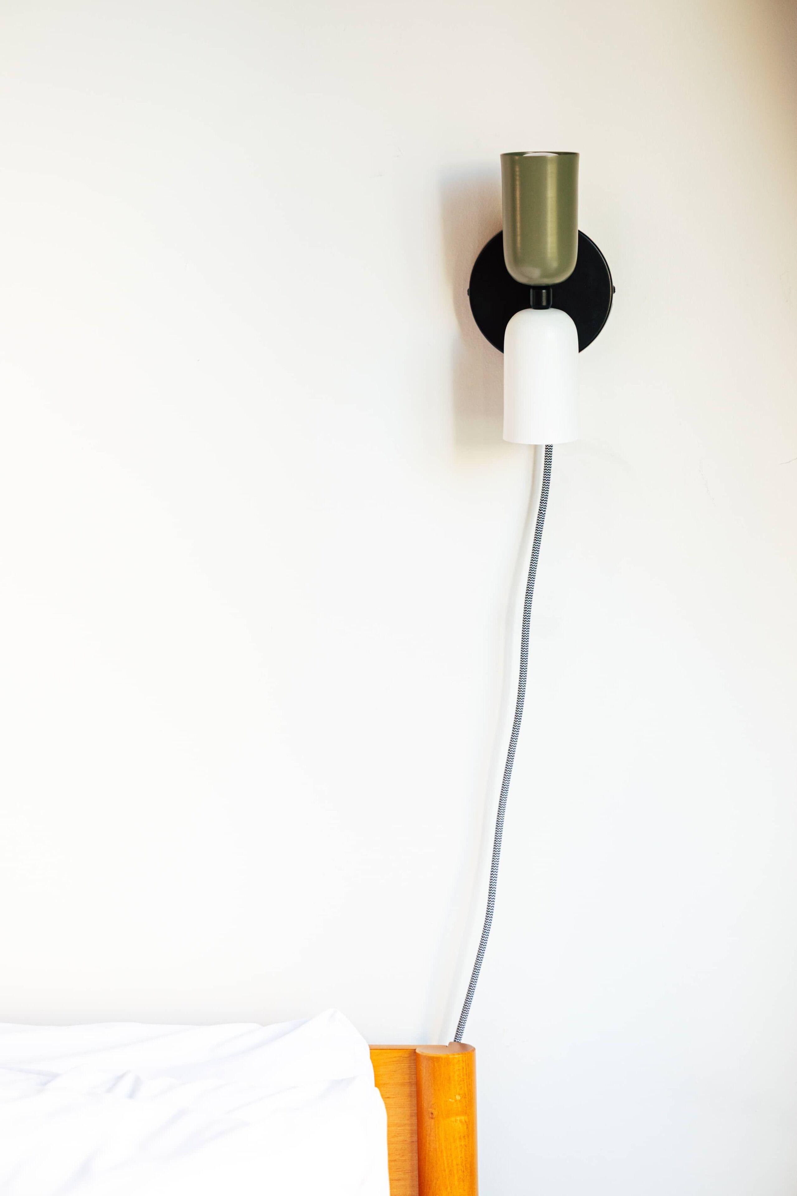 Un luminaire mural doté d’un abat-jour cylindrique et d’un cordon flexible.