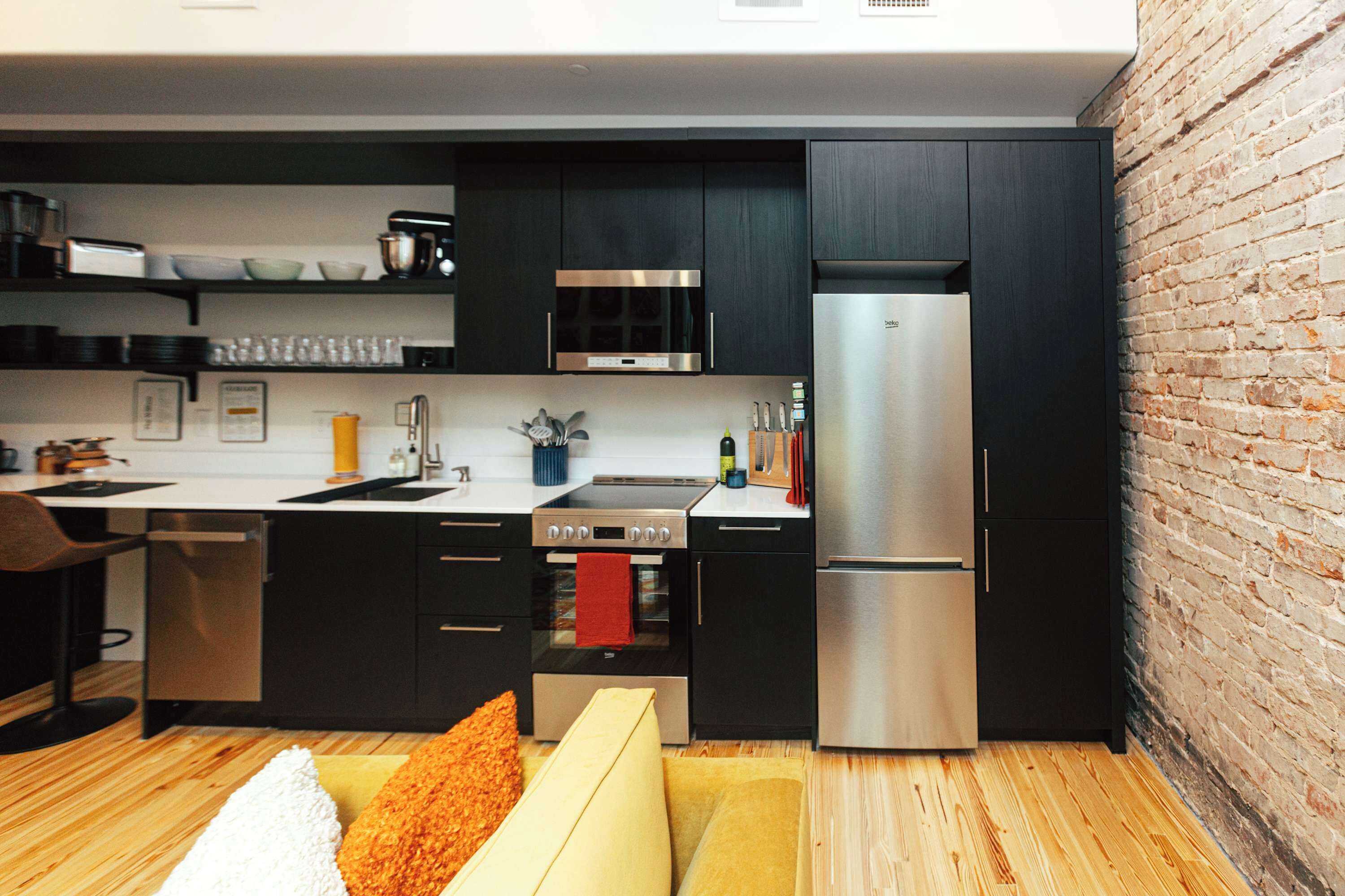 A modern kitchen with dark cabinetry, stainless steel appliances, and a brick wall.