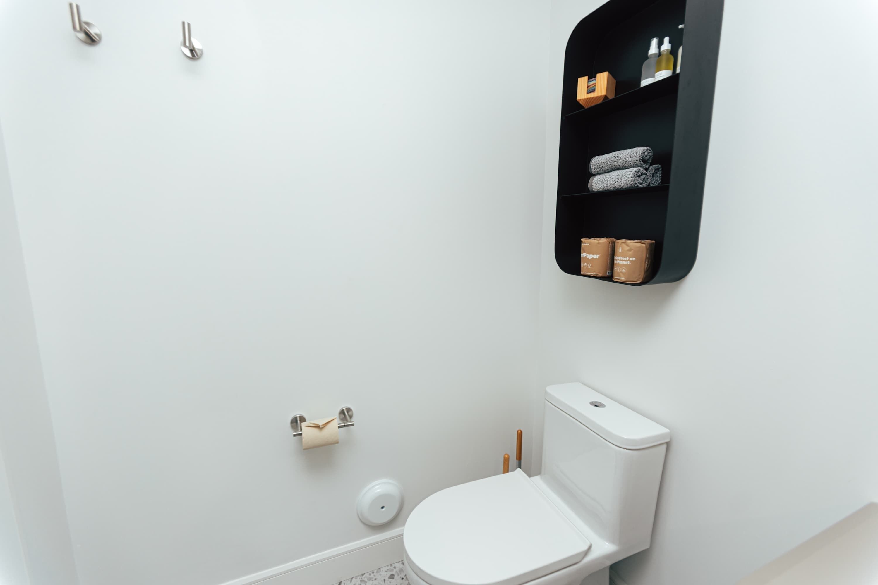 A modern bathroom with a white toilet, a black shelf with toiletries, and a toilet paper holder.