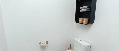 A modern bathroom with a white toilet, a black shelf with toiletries, and a toilet paper holder.