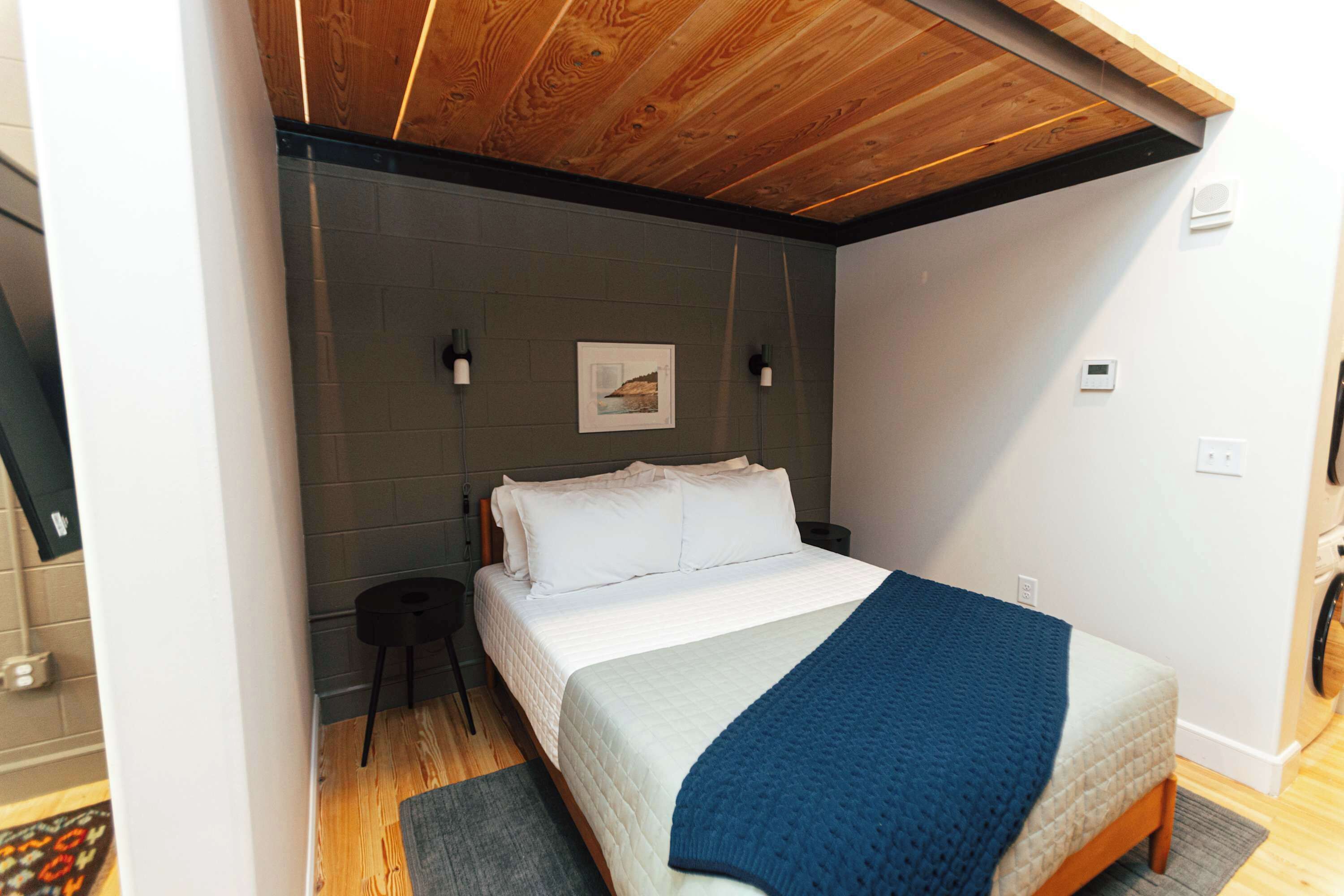Une chambre avec un plafond en bois, un lit avec une literie blanche, une couverture bleue et un petit tabouret.