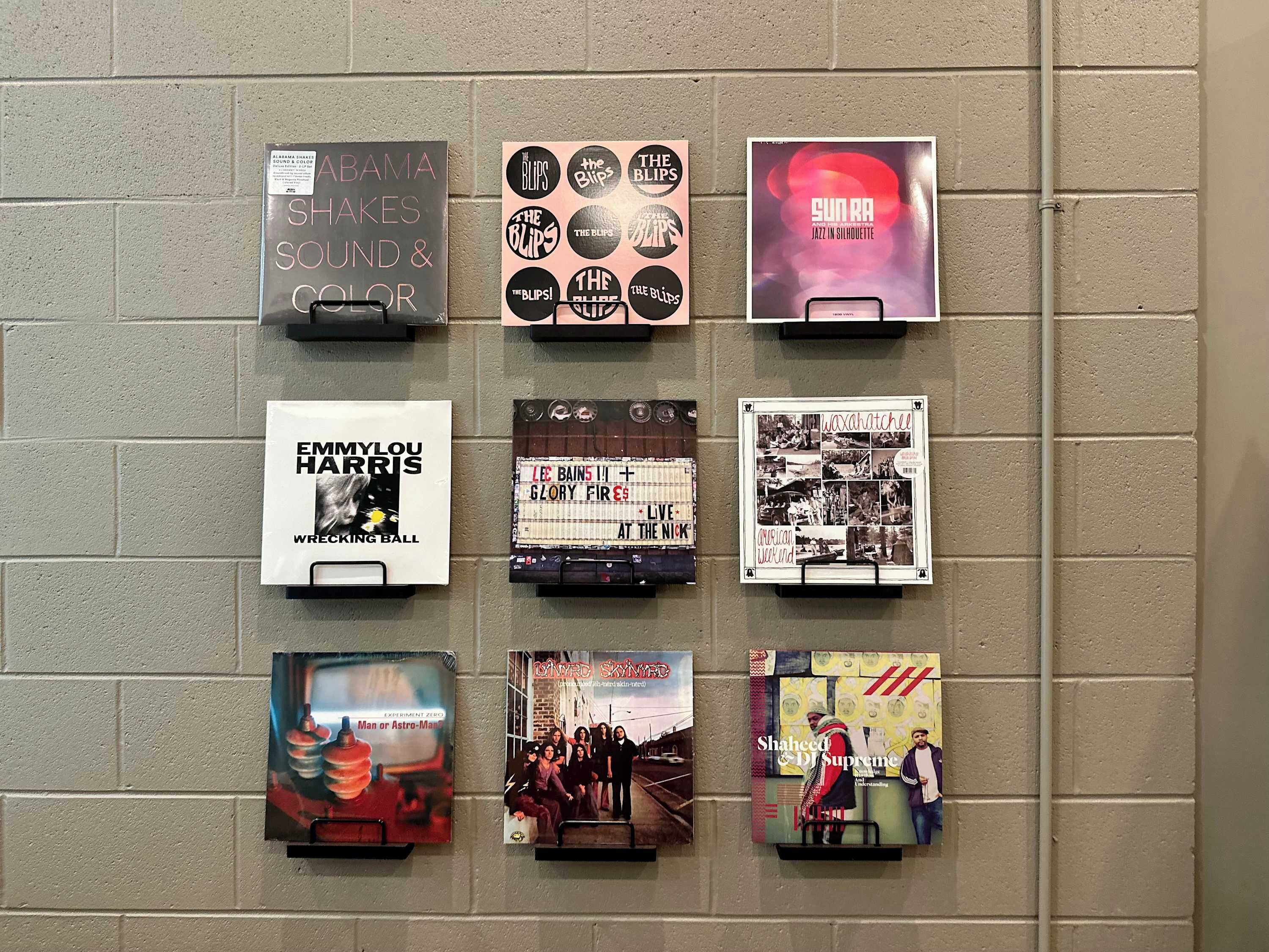 Una pared con nueve elementos enmarcados, incluyendo portadas de discos y carteles, probablemente relacionados con música o temas culturales.