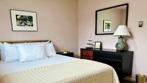 A neatly made bed with a quilted duvet, a bedside table with a lamp, a dresser with a mirror, and framed pictures on the wall. - Charming 2BR in Columbia Walkable Pet-friendly (Bellingham)