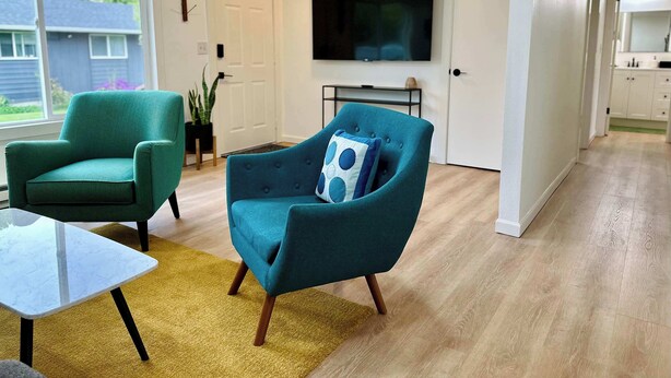 A modern living room with teal armchairs, a flat-screen TV, and a minimalist design. - Charming 2BR in Columbia Walkable Pet-friendly (Bellingham)