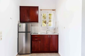 Eine Küche mit Edelstahlkühlschrank, Holzschränken, einem Fenster mit Vorhang und einer weißen Arbeitsplatte.