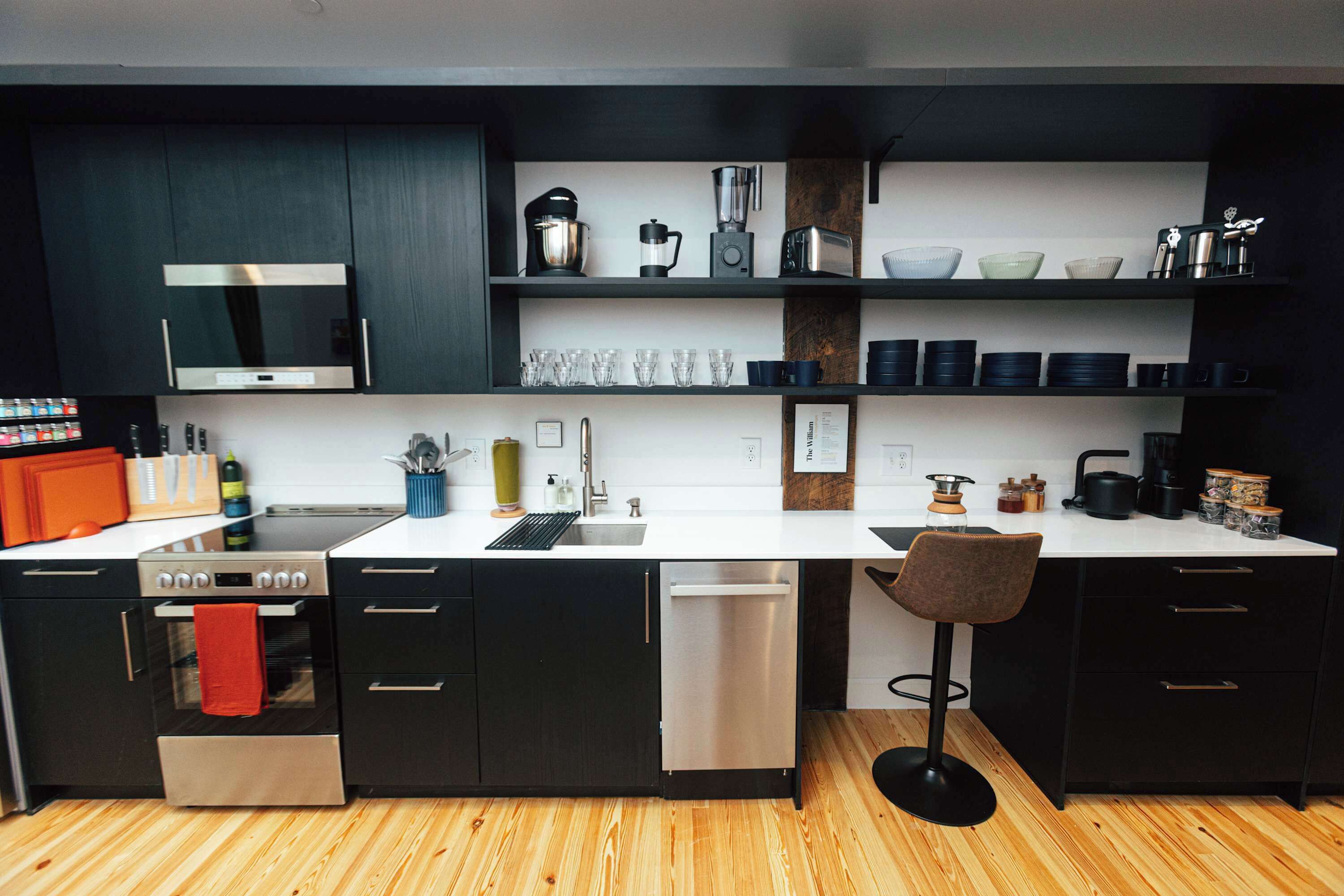 A modern kitchen with black cabinets, a white countertop, and stainless steel appliances.