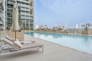 A rooftop pool with lounge chairs and umbrellas, surrounded by modern buildings and a clear sky. - Stayshort - Sophisticated JVC Apartment Sleeps 4 With Balcony (Dubai)