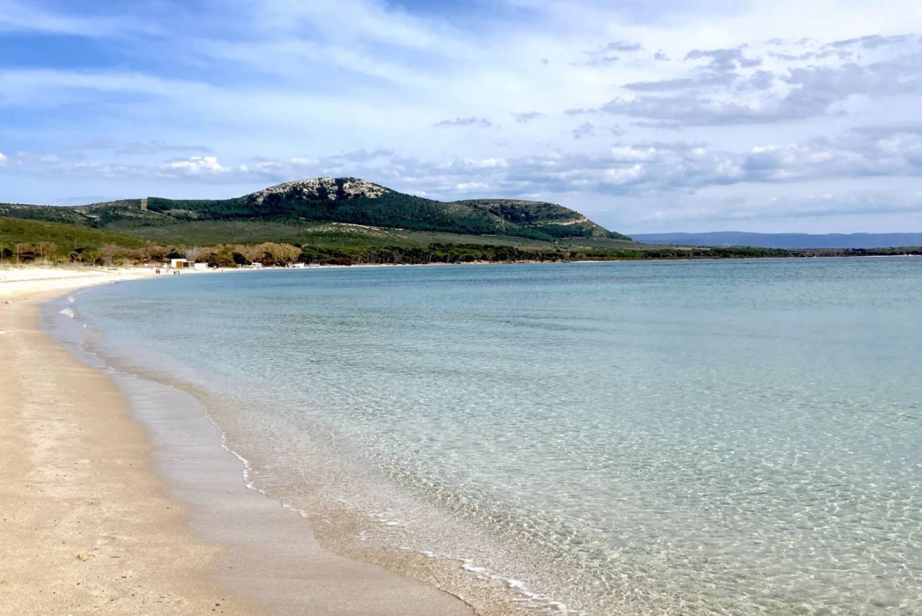 Una platja amb aigua cristal·lina, sorra daurada i una muntanya al fons.
