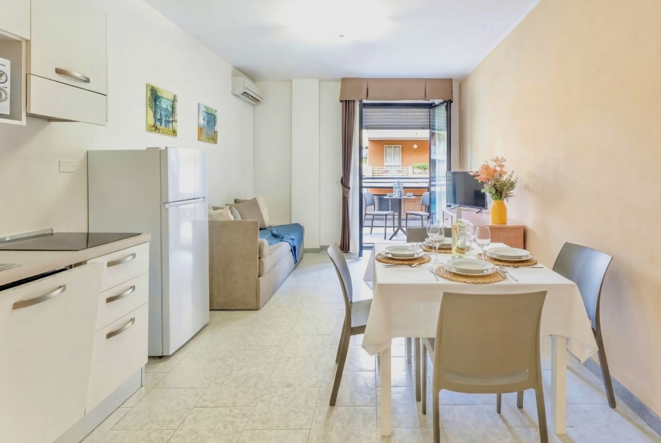 Una cucina moderna con frigorifero, fornello e pensili. C'è un'area pranzo con un tavolo apparecchiato per due e un divano sullo sfondo.