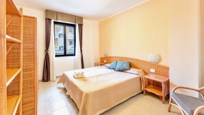 Hotellihuone, jossa on sänky, yöpöytä, tuoli ja ikkuna, jossa on verhot.