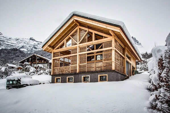 Eine Holzhütte mit geneigtem Dach, großen Fenstern und verschneiter Landschaft.
