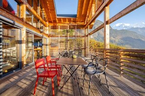 Eine Holzterrasse mit Tisch und Stühlen, mit Blick auf eine gebirgige Landschaft.
