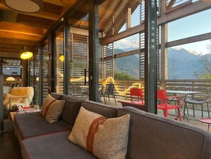 Un interior acogedor con un sofá, sillones y ventanas amplias con vistas a un paisaje montañoso.