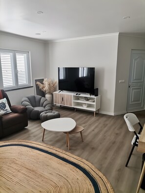 Uma sala de estar moderna com uma televisão de tela plana, um sofá, uma mesa de centro e uma área de jantar com cadeiras.
