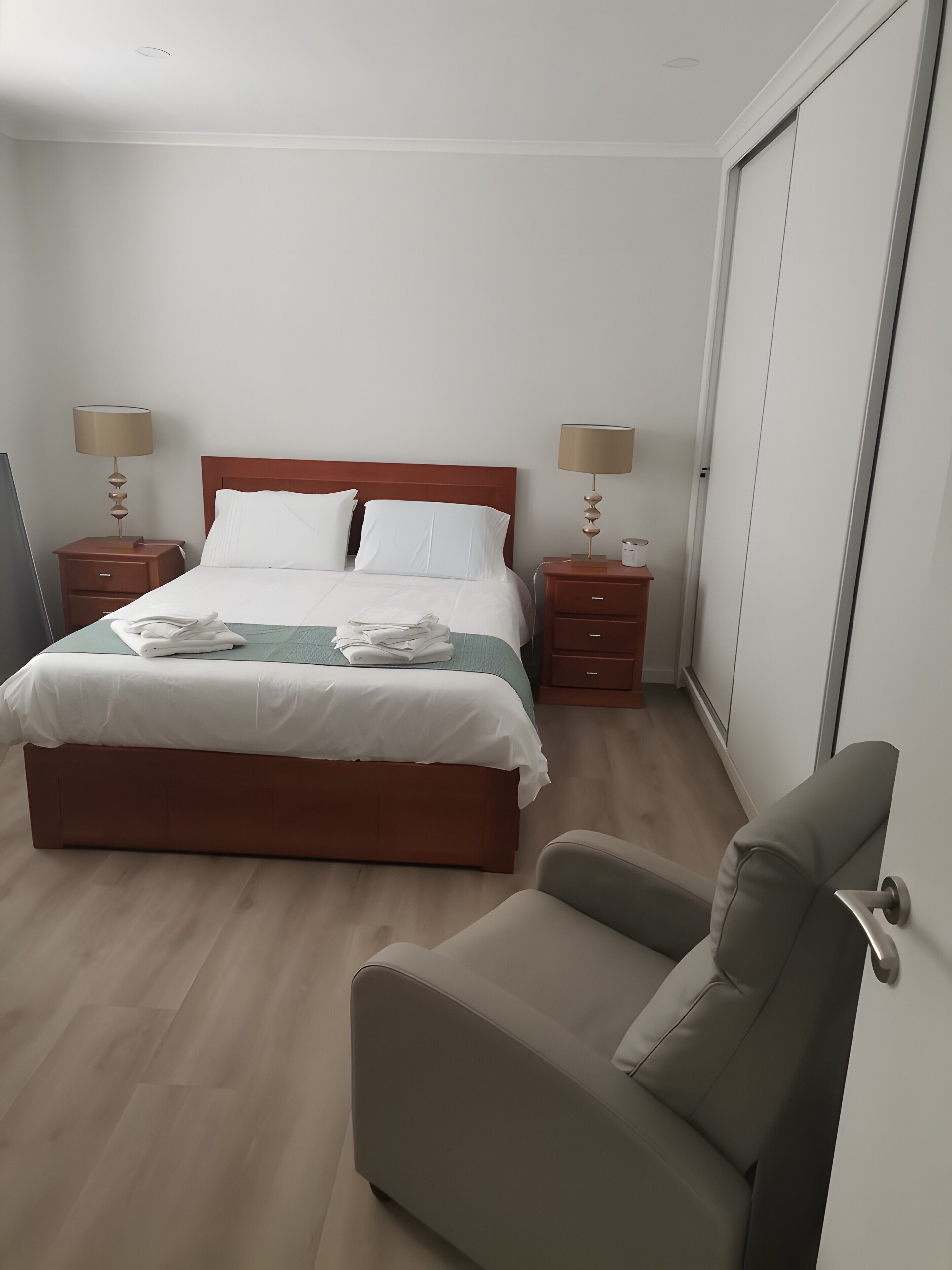 Habitació d'hotel ordenada amb llit, dues taules de nit amb làmpades, una cadira i un armari.