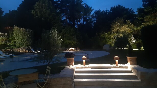 Una escalera de piedra conduce a un área de piscina con mobiliario exterior y una pérgola.