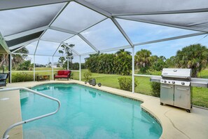 A covered swimming pool with a grill and outdoor furniture.