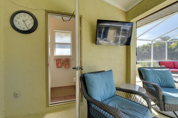 A room with wicker chairs, a flat-screen TV, and a wall clock.
