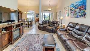 A spacious living room with a leather sofa, a dining area with a chandelier, and a large painting on the wall. - Beach Days & Fairways: Rotonda West Snowbird Home (Rotonda West)