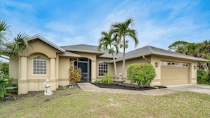 A single-story house with a garage, a front yard with a palm tree, and a small garden area. - Beach Days & Fairways: Rotonda West Snowbird Home (Rotonda West)