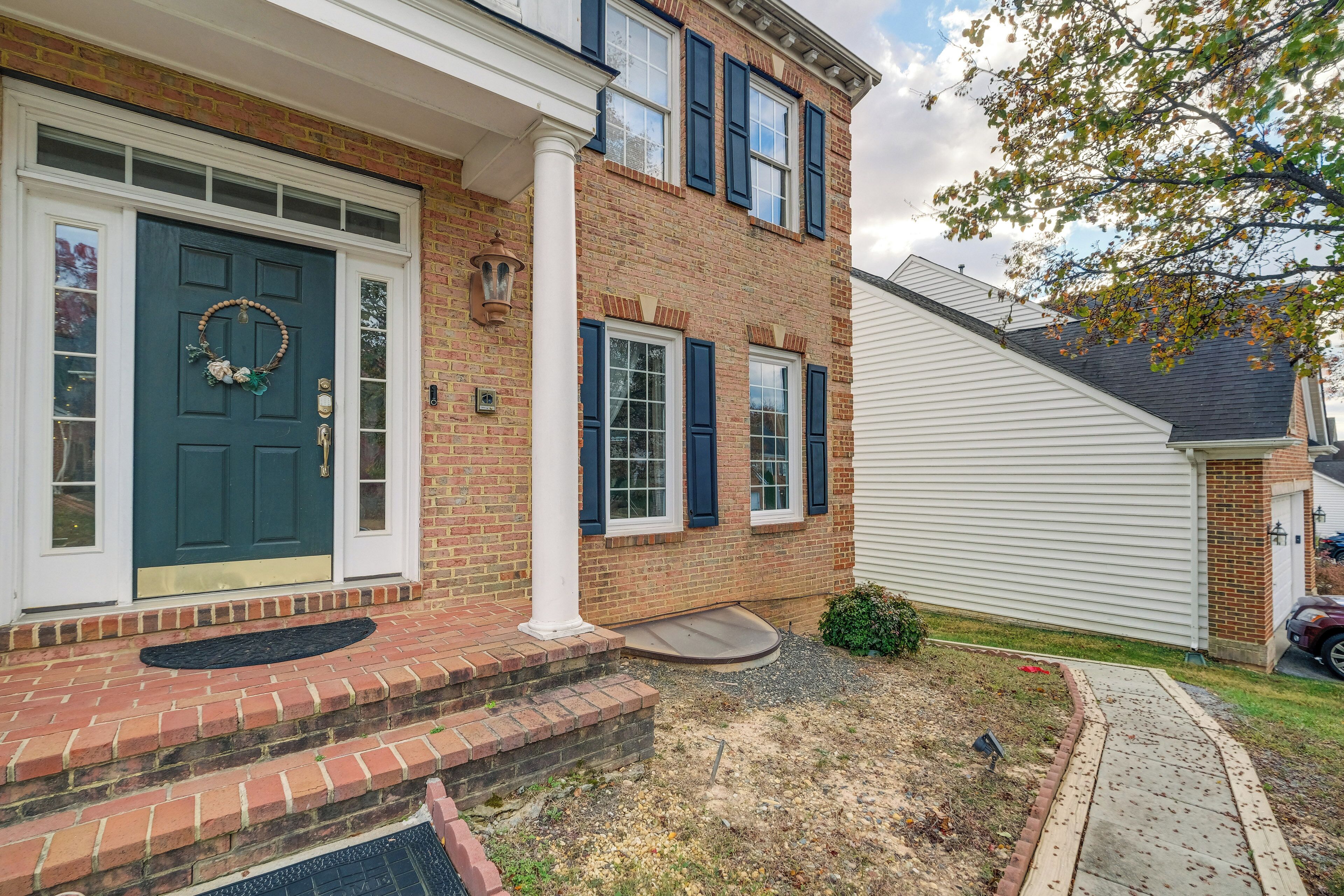 A two-story brick house with a dark green front door, white shutters, and a small porch with steps.