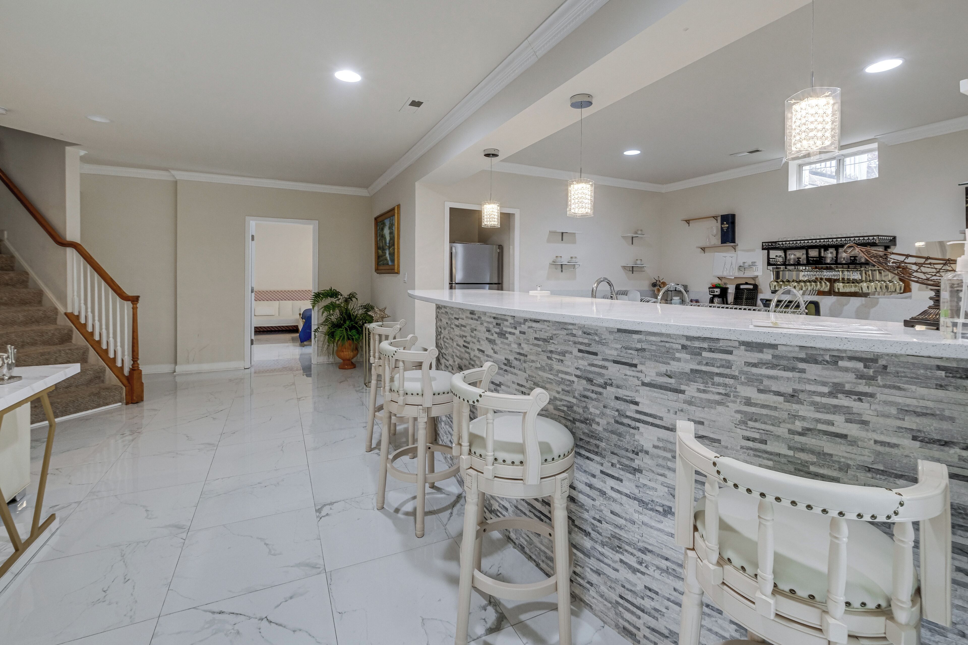 A modern kitchen with a marble countertop, bar stools, and a built-in refrigerator.