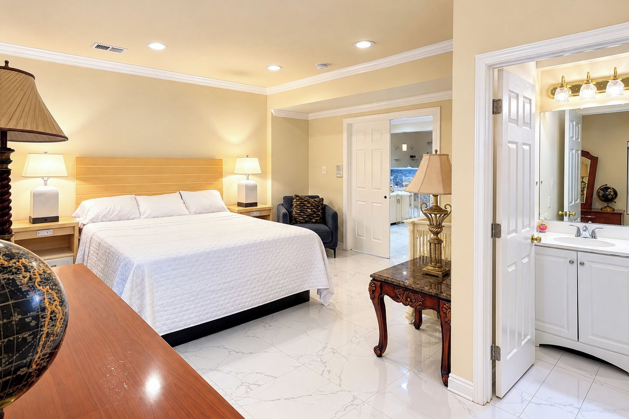 A hotel room with a large bed, a desk, a chair, a vanity with a mirror, and a globe on the desk.