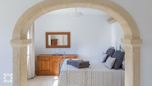 Ein Schlafzimmer mit einem Steingewölbe, einem Holzschrank, einem Bett mit gemusterten Betttextilien und einem Spiegel an der Wand.