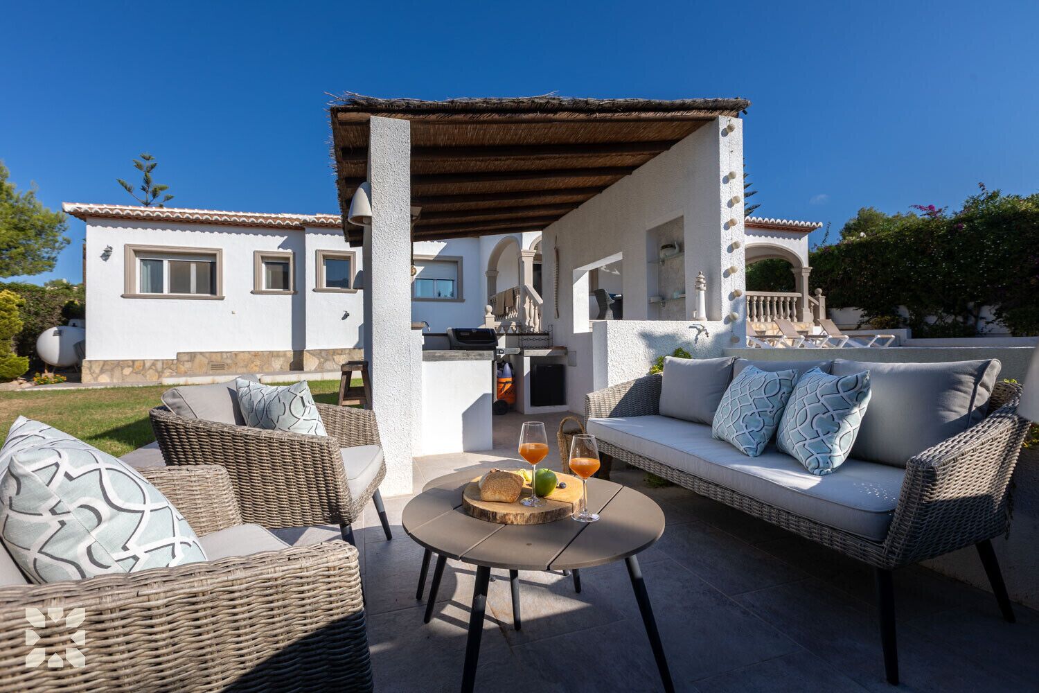 Een terras met rieten meubels, een ronde tafel en een pergola.