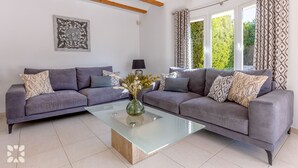 Ein Wohnzimmer mit zwei grauen Sofas, einem Glastisch und Kissen mit Muster.