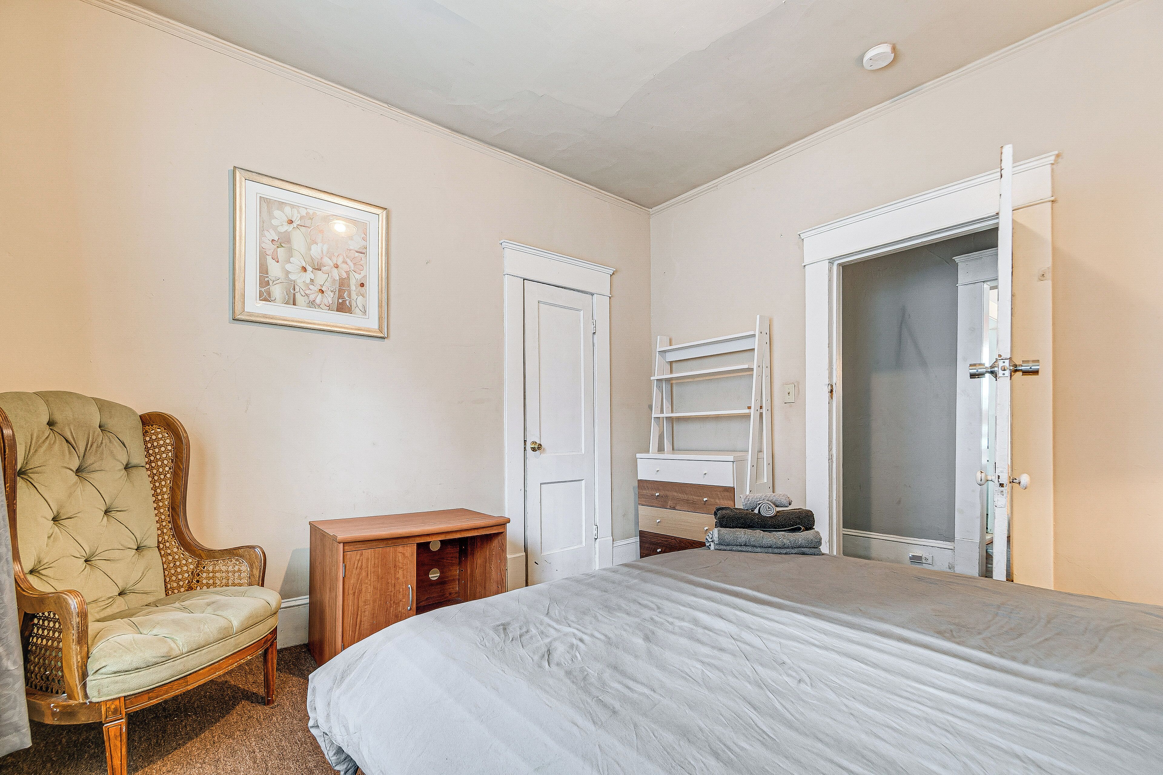 Ein Schlafzimmer mit einem Bett, einem Sessel, einem Kleiderschrank und einer Tür.