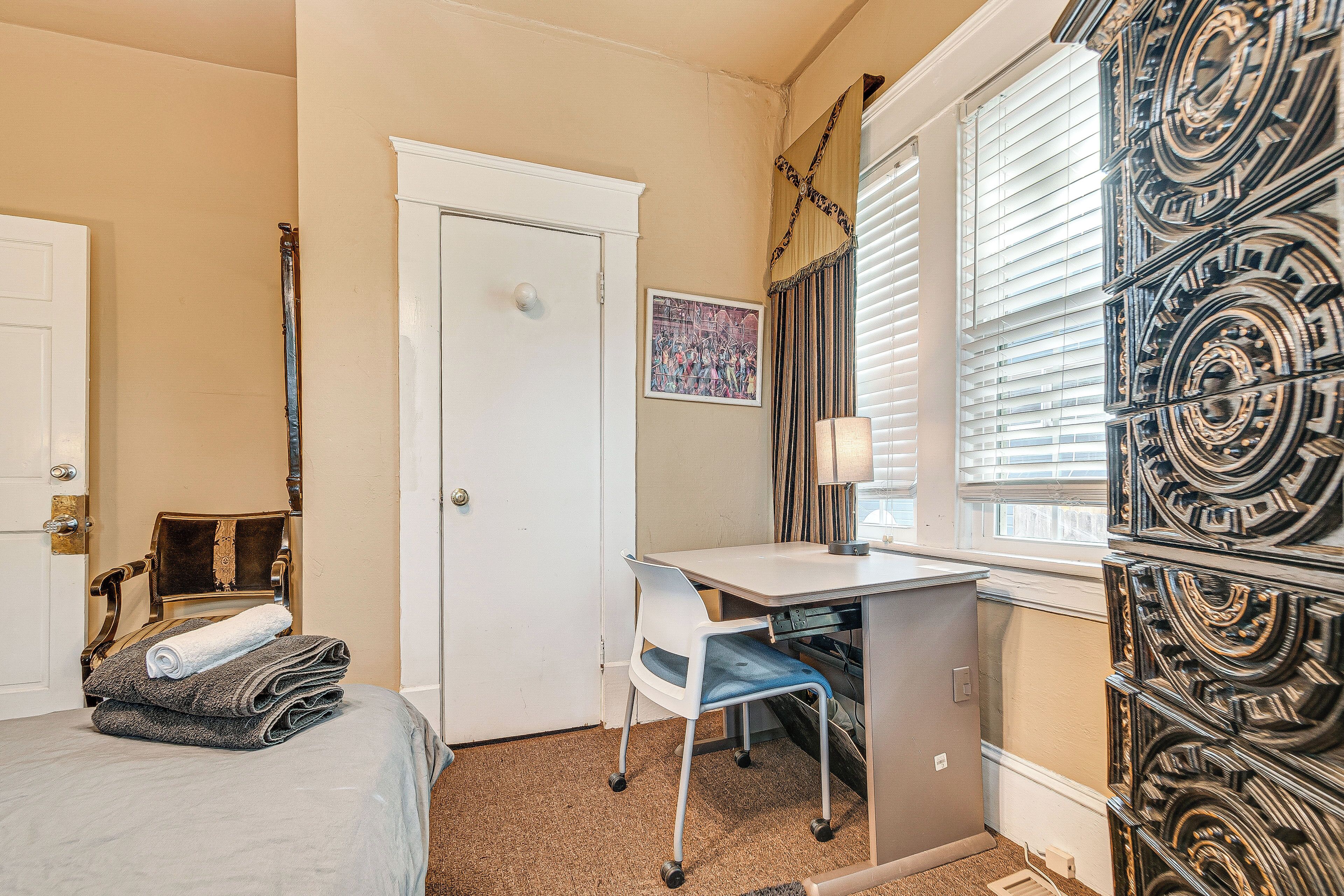 A hotel room with a bed, a desk, a chair, a door, and a window with blinds.
