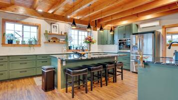 A spacious kitchen with wooden beams, green cabinets, a central island with stools, and a stainless steel refrigerator.