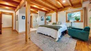 A spacious bedroom with a large bed, a green armchair, wooden beams on the ceiling, and a window with plants. - Big Groups Welcome! Mtn-view Onalaska Estate (Onalaska)