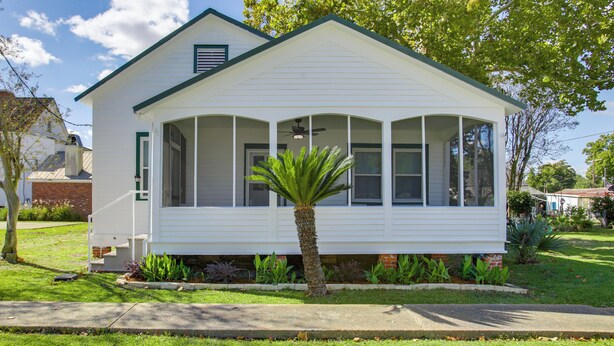 Een gelijkvloers huis met veranda, een kleine palmboom en een fundering van baksteen.