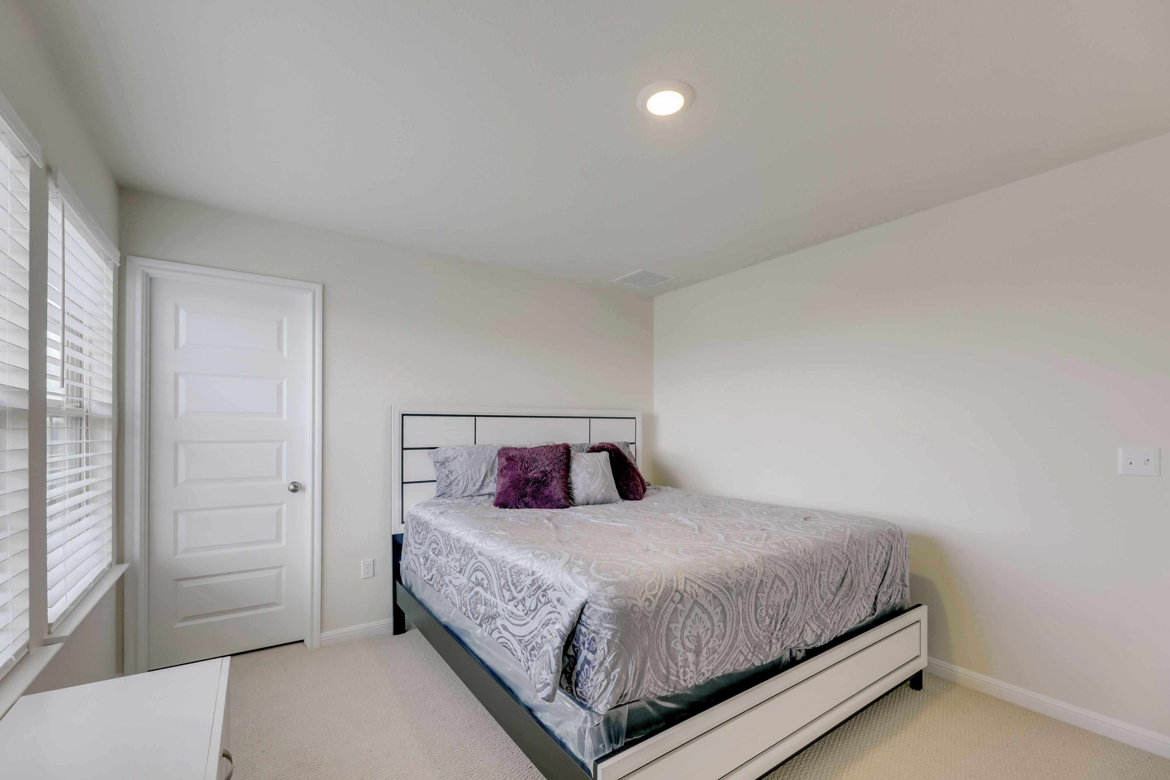 A bedroom with a bed, a door, and a window with blinds.