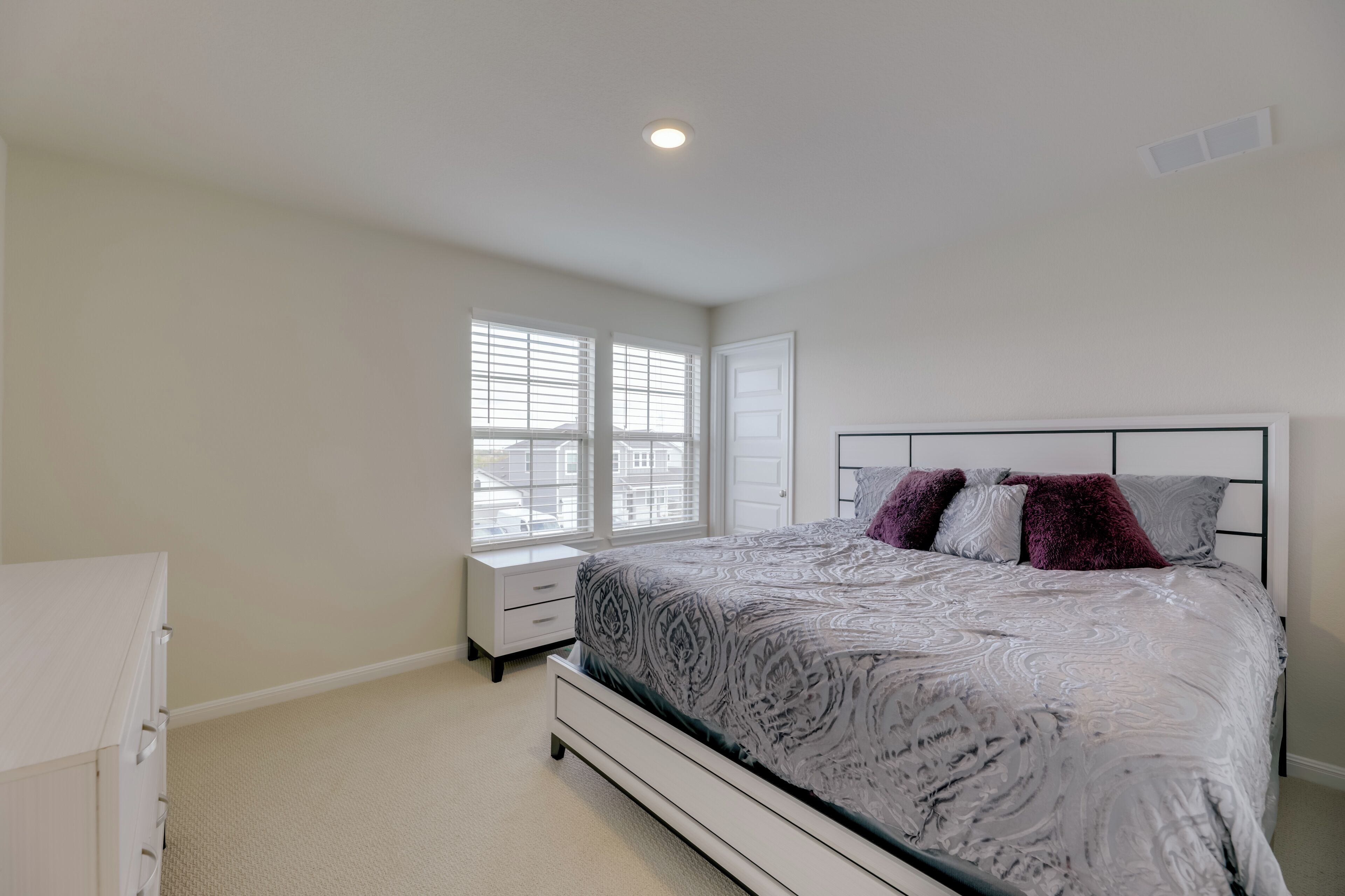 A bedroom with a bed, a nightstand, a dresser, and a window with blinds.