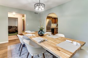 A dining area with a wooden table, white chairs, a vase with flowers, and a chandelier.