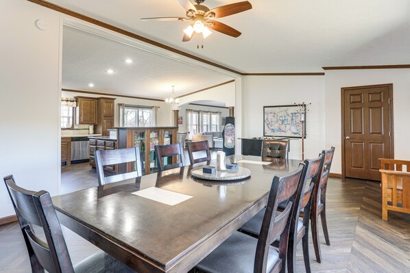 A spacious dining area with a large wooden table and chairs, a ceiling fan, and a view into the kitchen. - Fish & Relax Fireside: Mink Lake Retreat! (Buffalo)