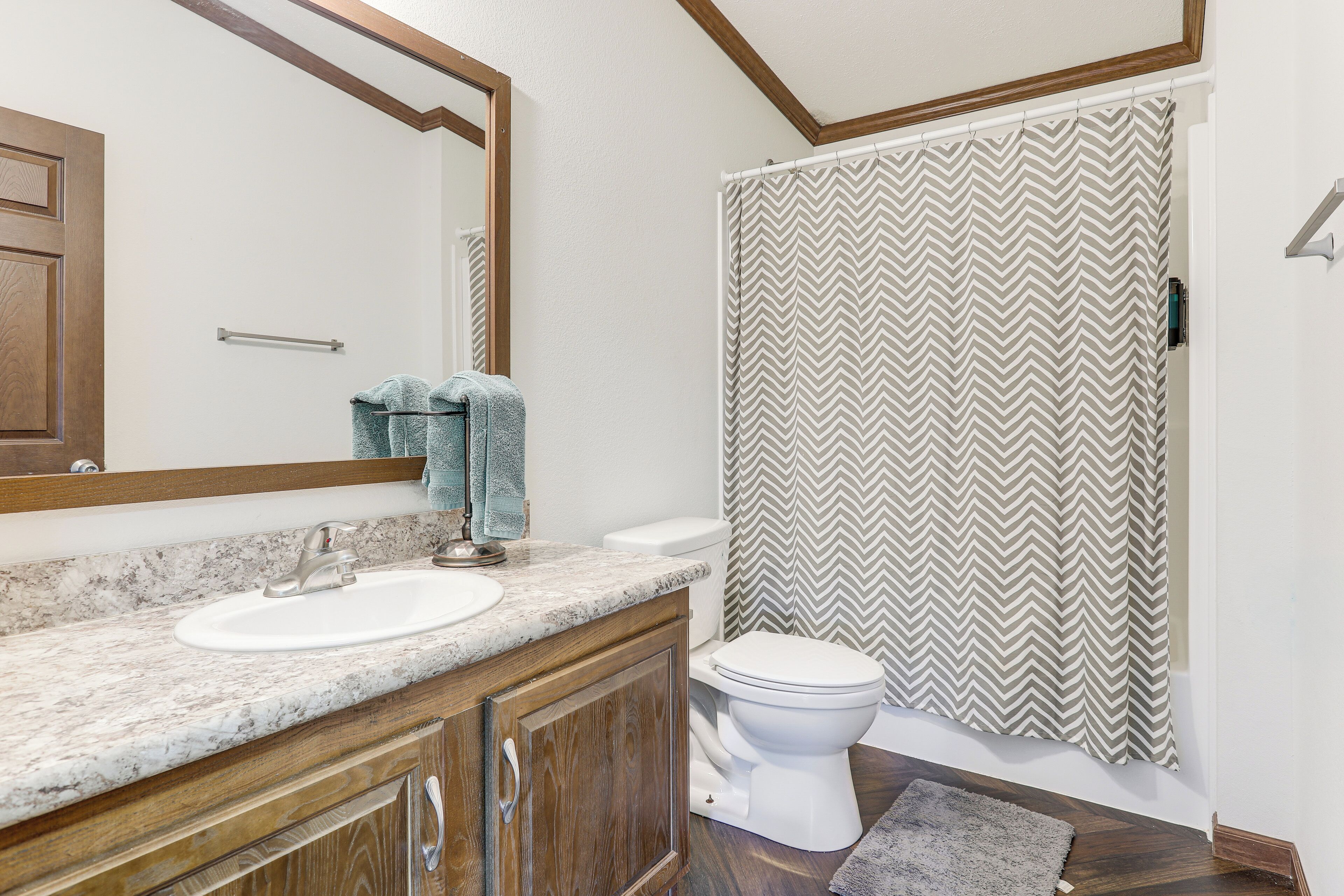A bathroom with a marble sink, wooden cabinets, a white toilet, and a shower with a chevron-patterned curtain.