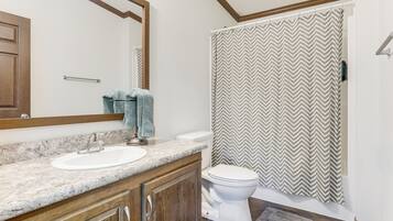 A bathroom with a marble sink, wooden cabinets, a white toilet, and a shower with a chevron-patterned curtain.