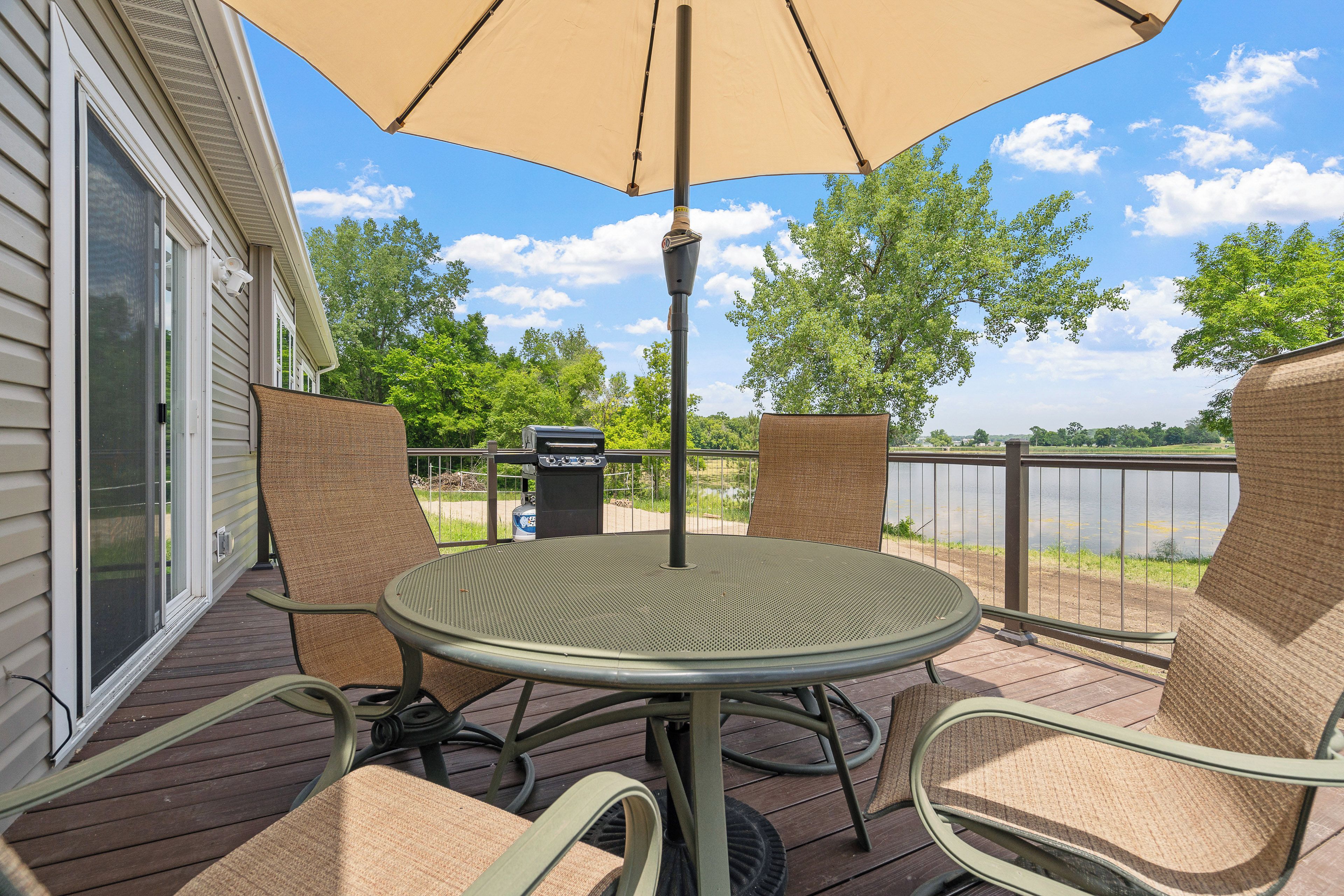 A patio with a round table and chairs, an umbrella, and a view of a lake.