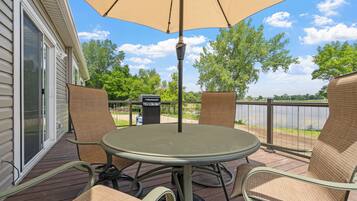 A patio with a round table and chairs, an umbrella, and a view of a lake.
