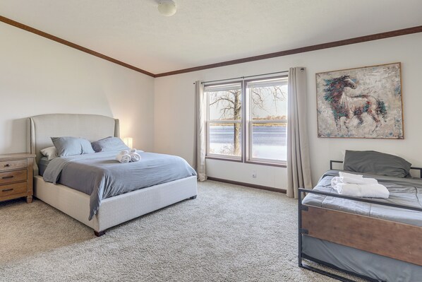 A bedroom with a bed, a nightstand, a window with a view, and a painting on the wall. - Fish & Relax Fireside: Mink Lake Retreat! (Buffalo)