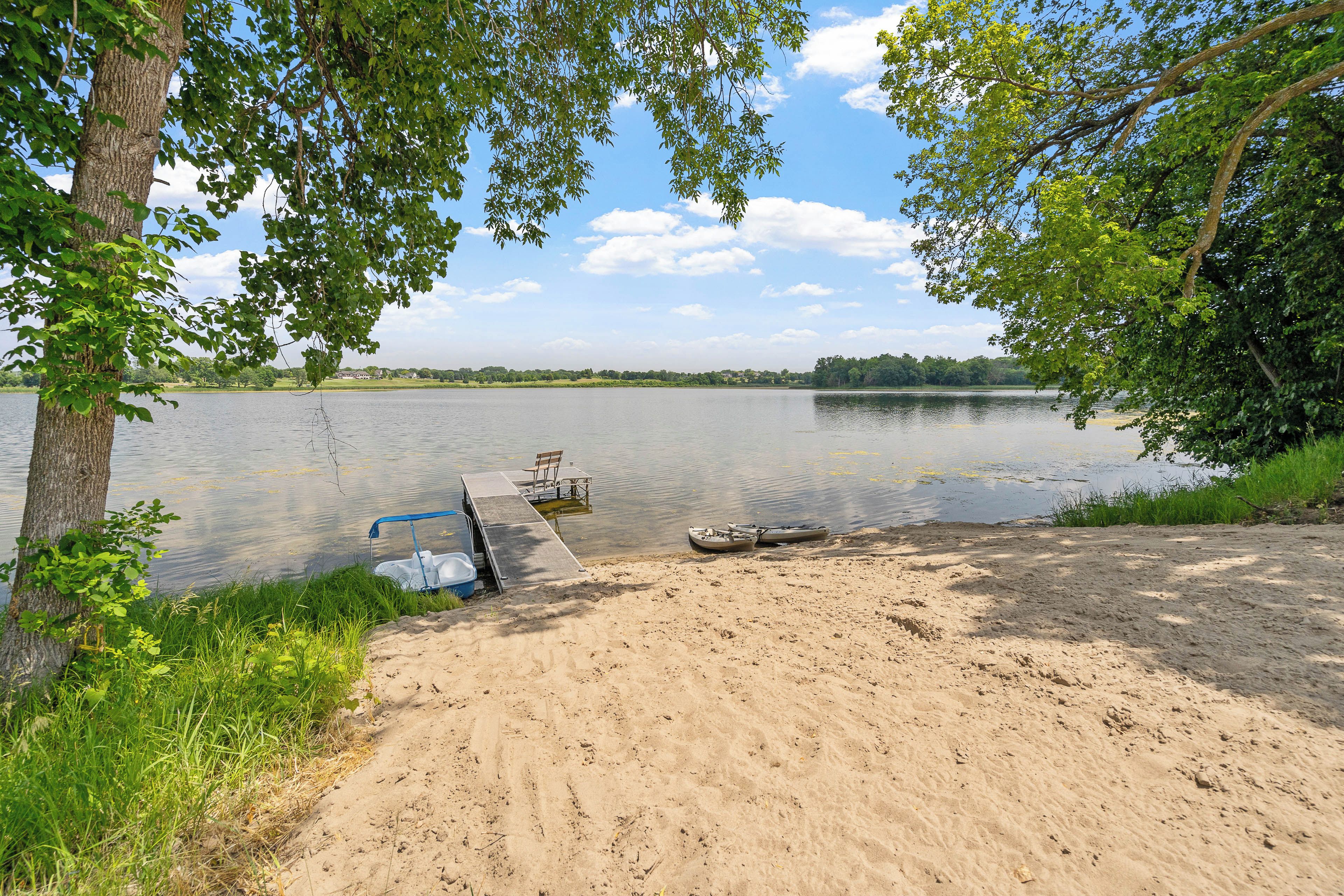 A lakeside setting with a sandy beach, a dock, and kayaks.